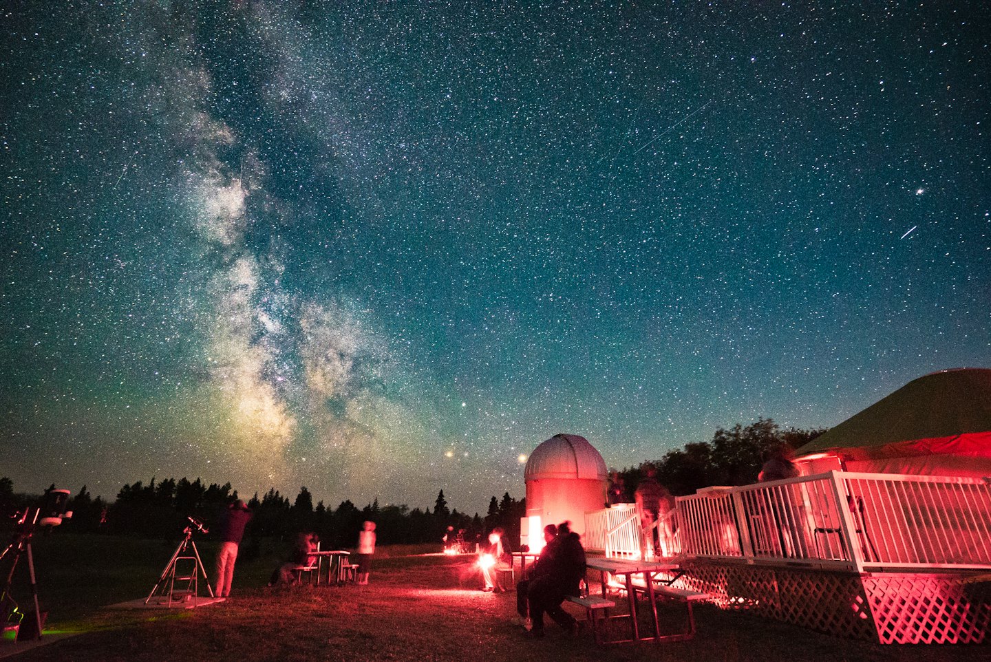 People use telescopes to stargaze at an observatory under the Milky Way.